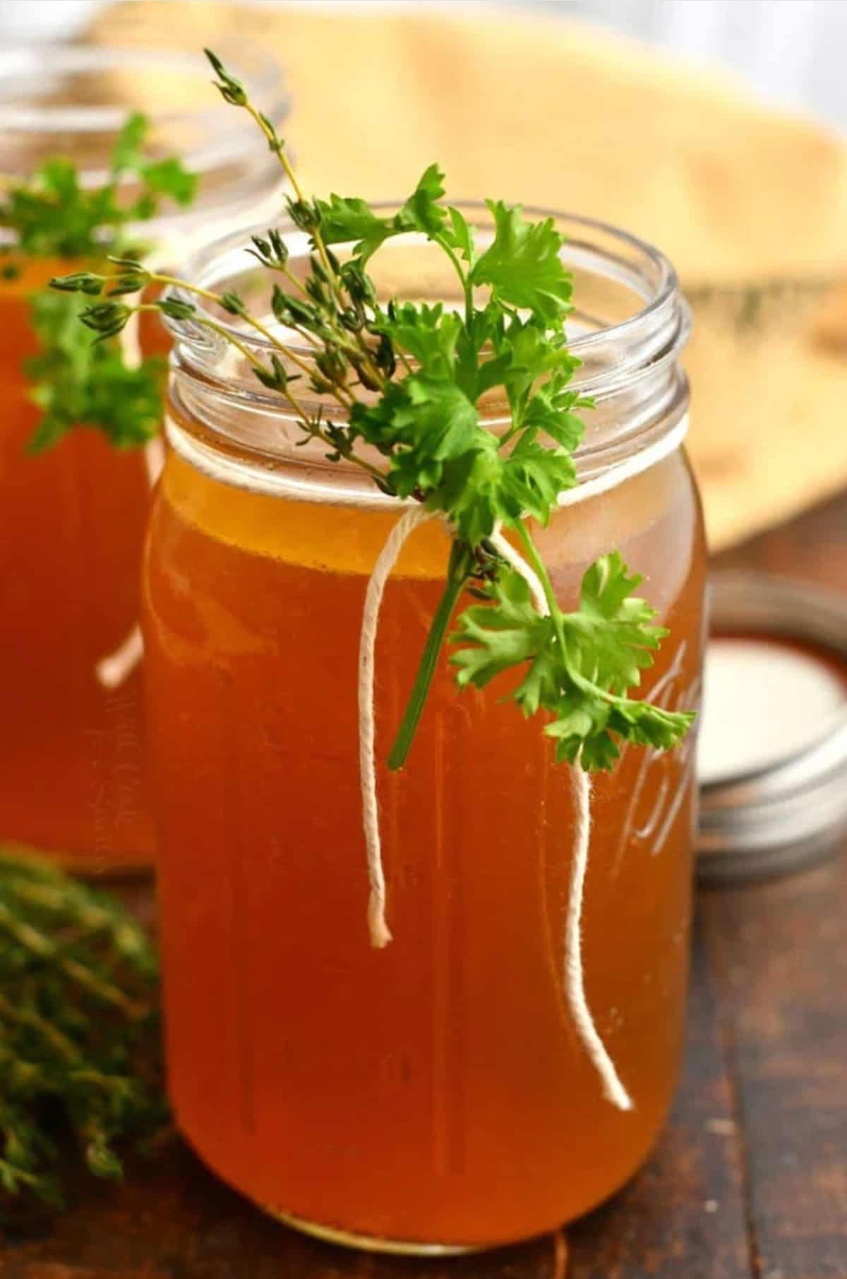 homemade beef stock in glass mason jars with some herbs tied to it.