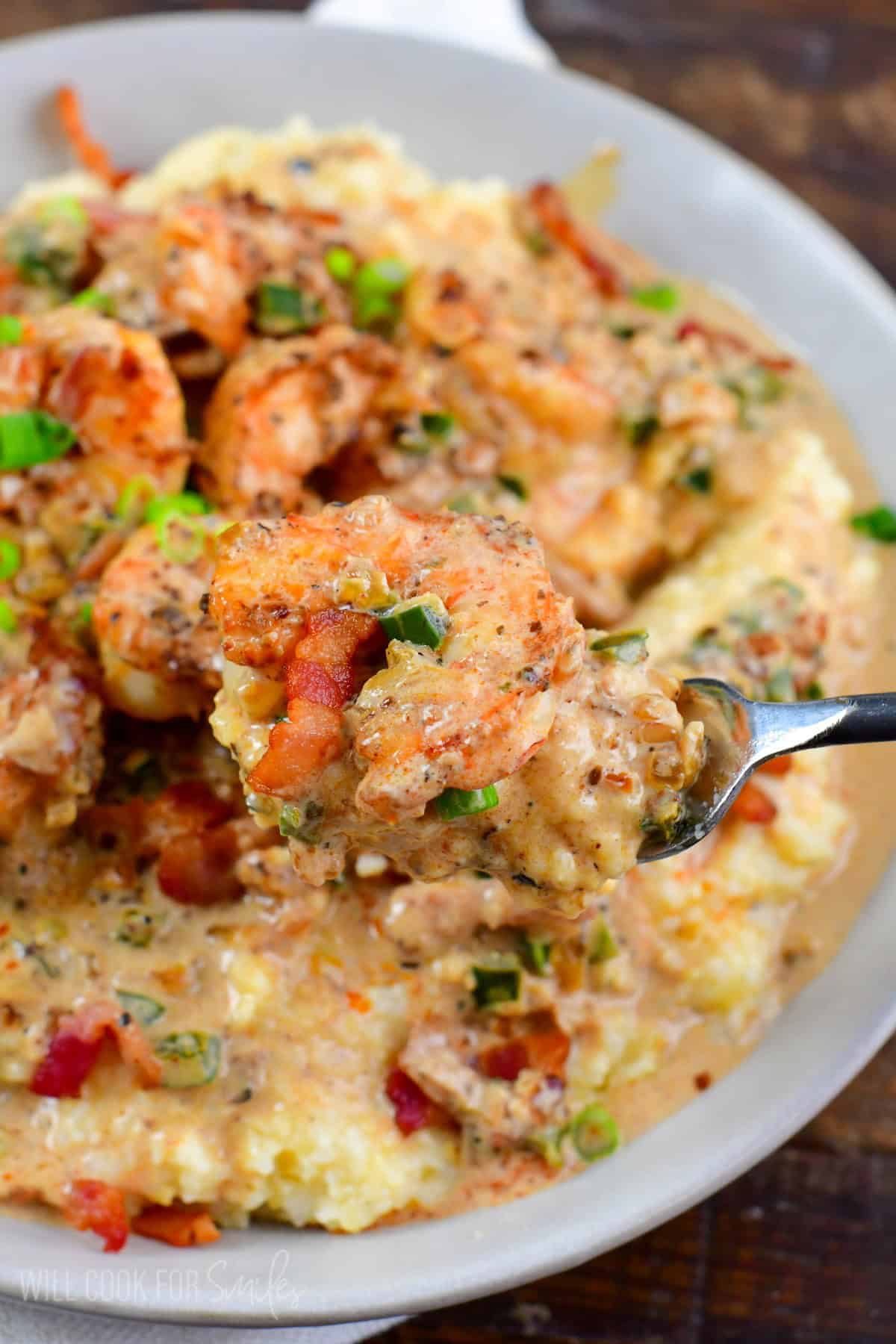 holding some creamy Cajun shrimp and grits on a fork over the bowl.