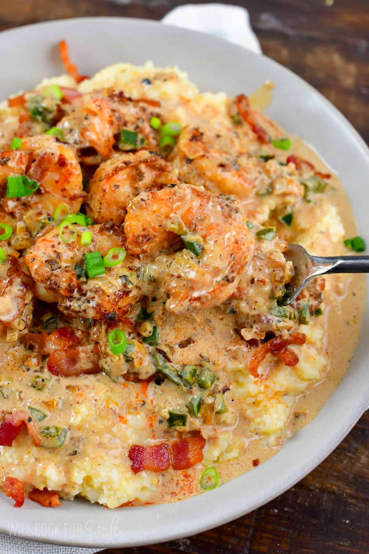 Scooping out some Cajun shrimp with creamy sauce from the bowl.