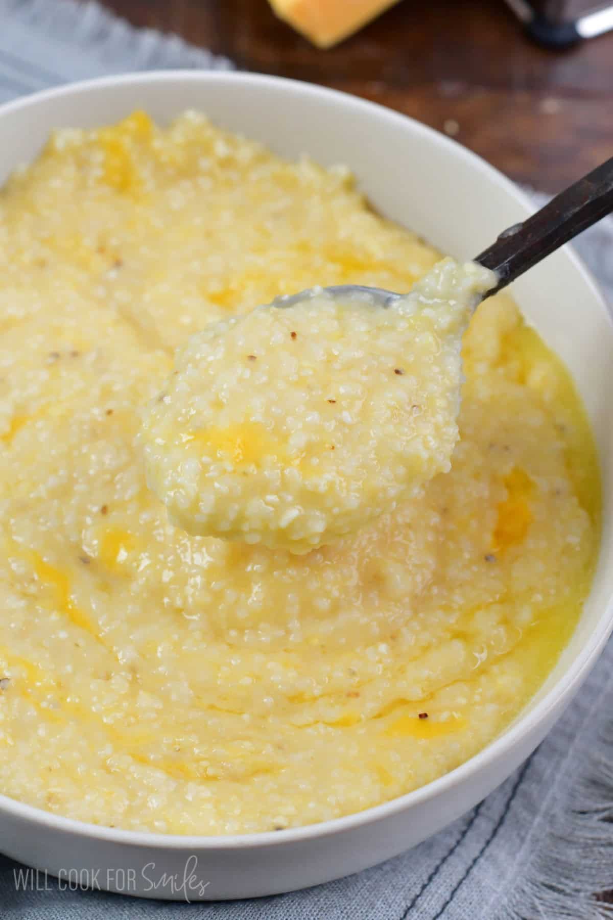 holding some cheesy grits in a spoon over the bowl.