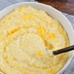 stirring cheesy grits in a bowl with a spoon.