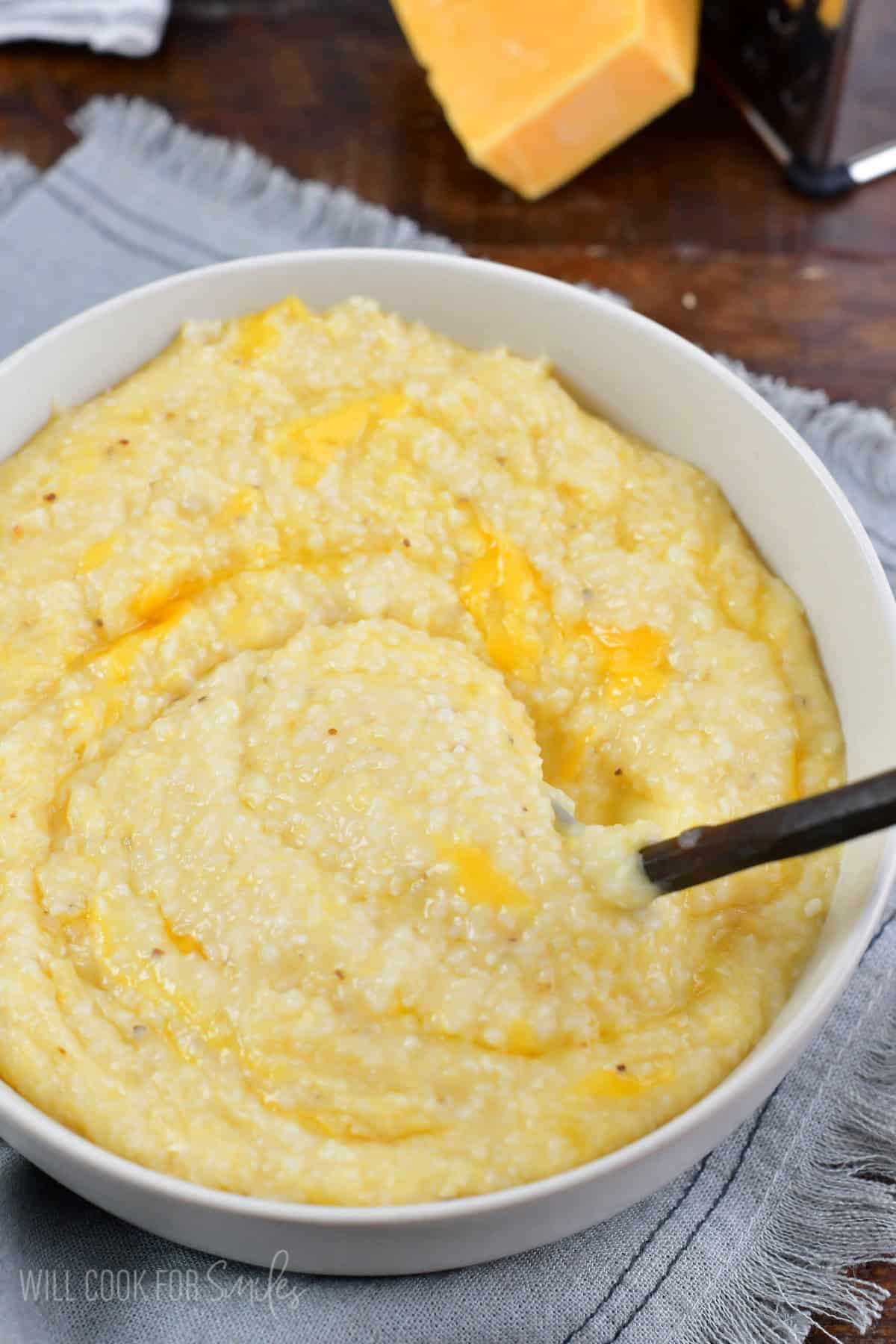 stirring cheesy grits in a bowl with a spoon.