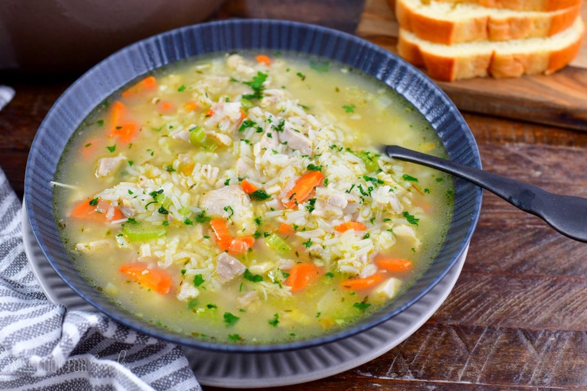 Bowl of chicken and rice soup with a spoon and a plate underneath the bowl.