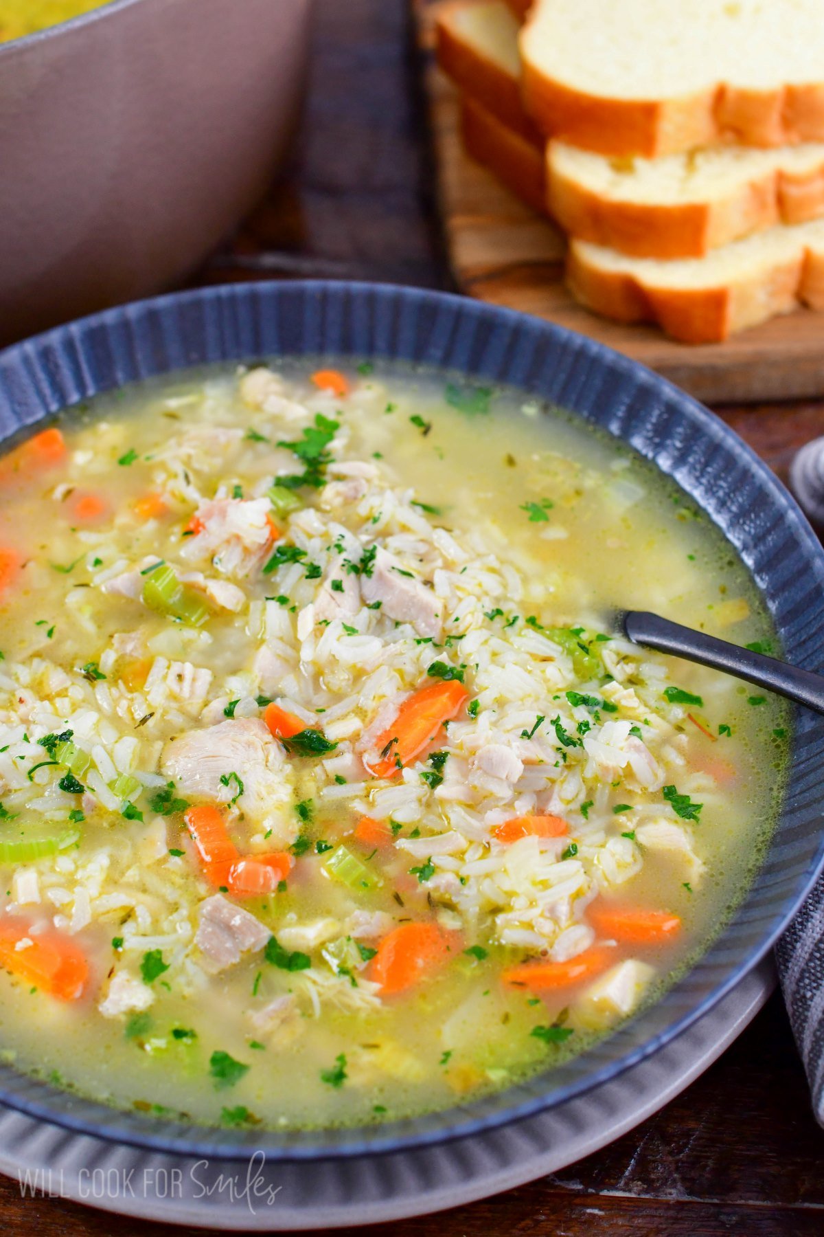 Chicken and rice soup in a bowl with a spoon on a wood surface.