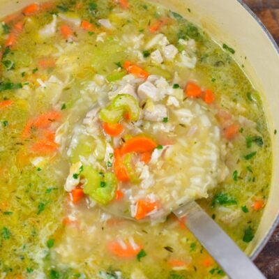 Scooping chicken and rice soup out of a pot with a metal ladle.