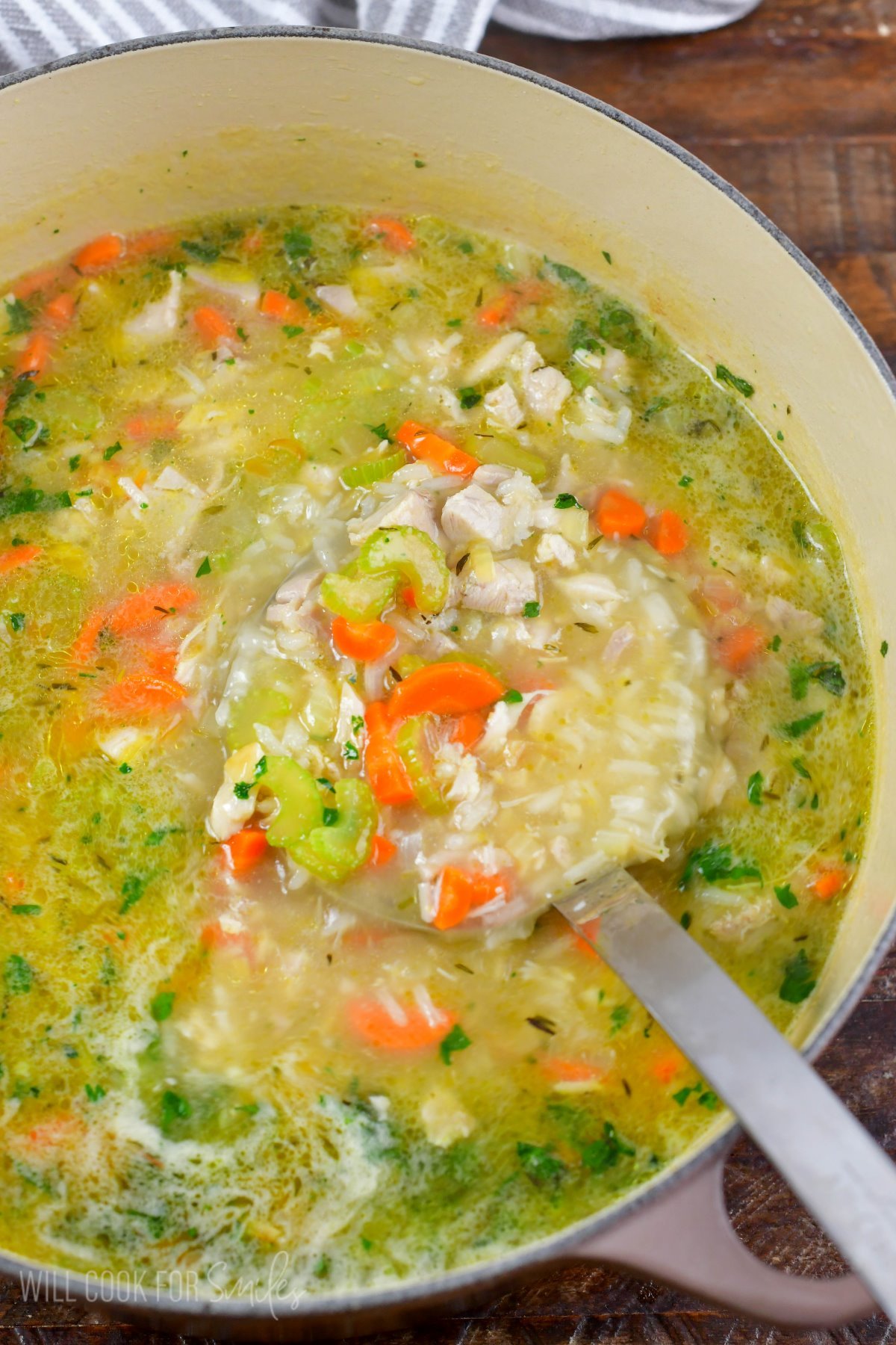 Scooping chicken and rice soup out of a pot with a metal ladle.