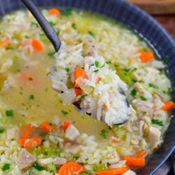 Chicken and rice soup in a bowl with a spoon scooping some of the soup up.