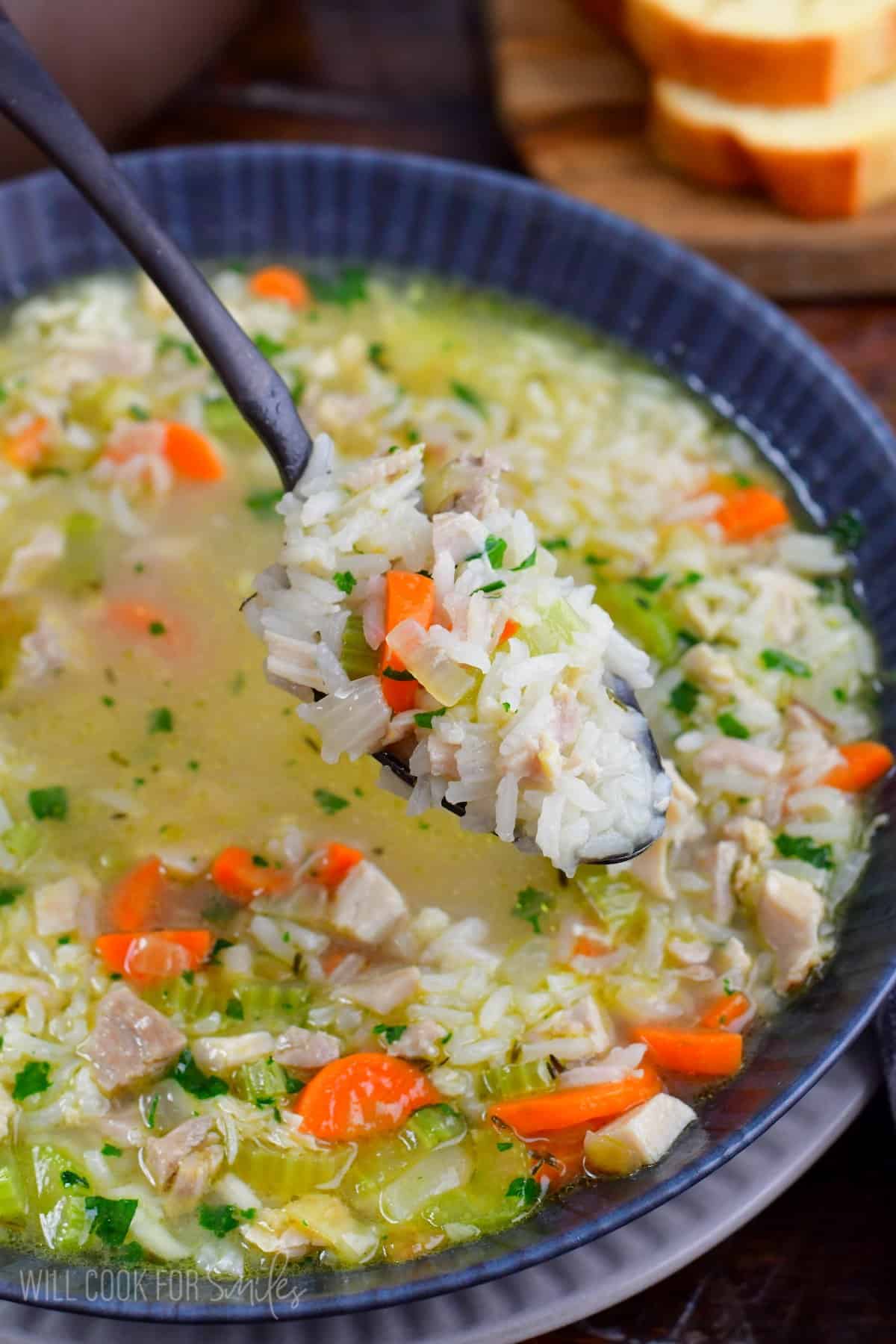 Chicken and rice soup in a bowl with a spoon scooping some of the soup up.