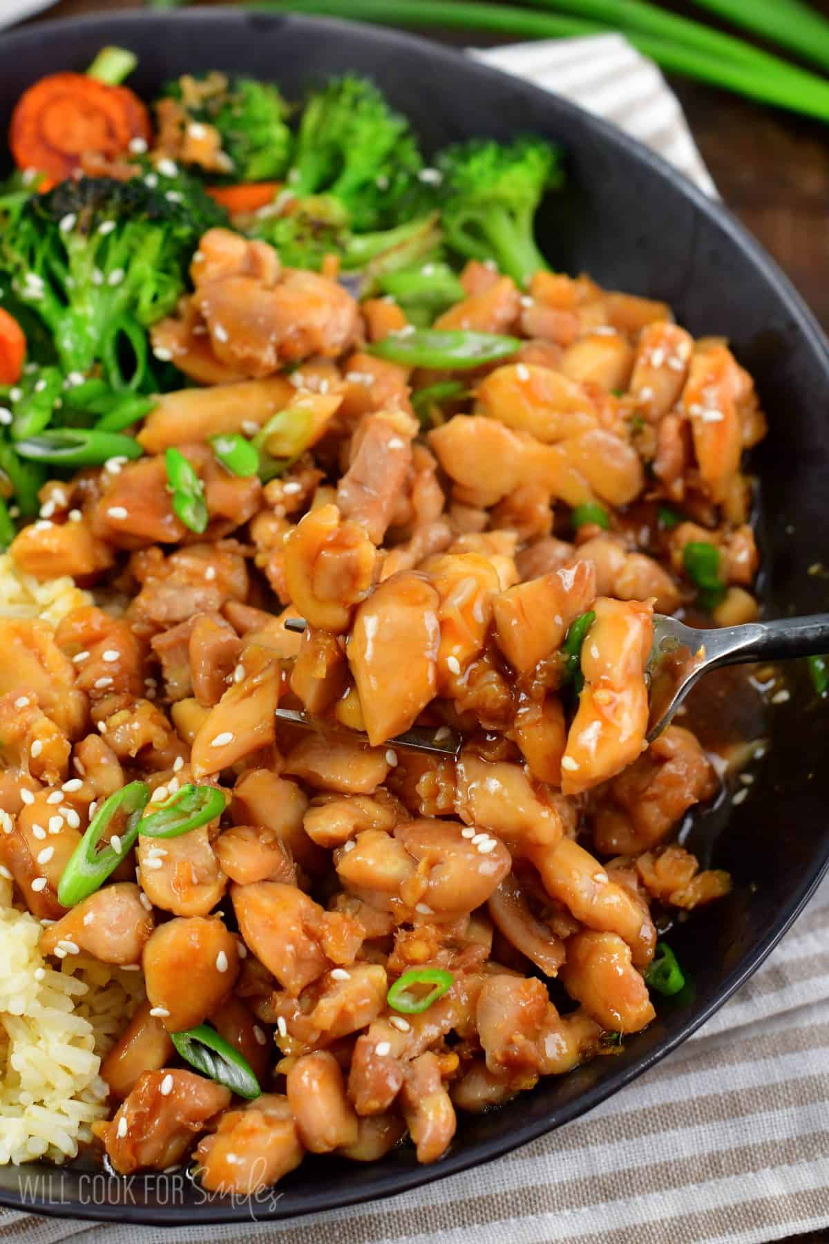 scooping some chicken teriyaki from a bowl with a fork.