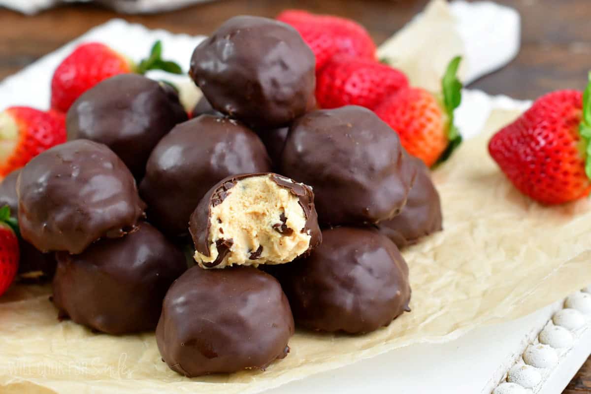 chocolate covered peanut butter cheesecake bites with one bite taken out next to strawberries.