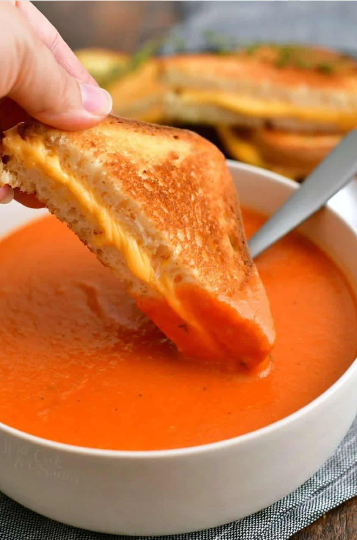 dipping a triangle of grilled cheese into a bowl of tomato soup.