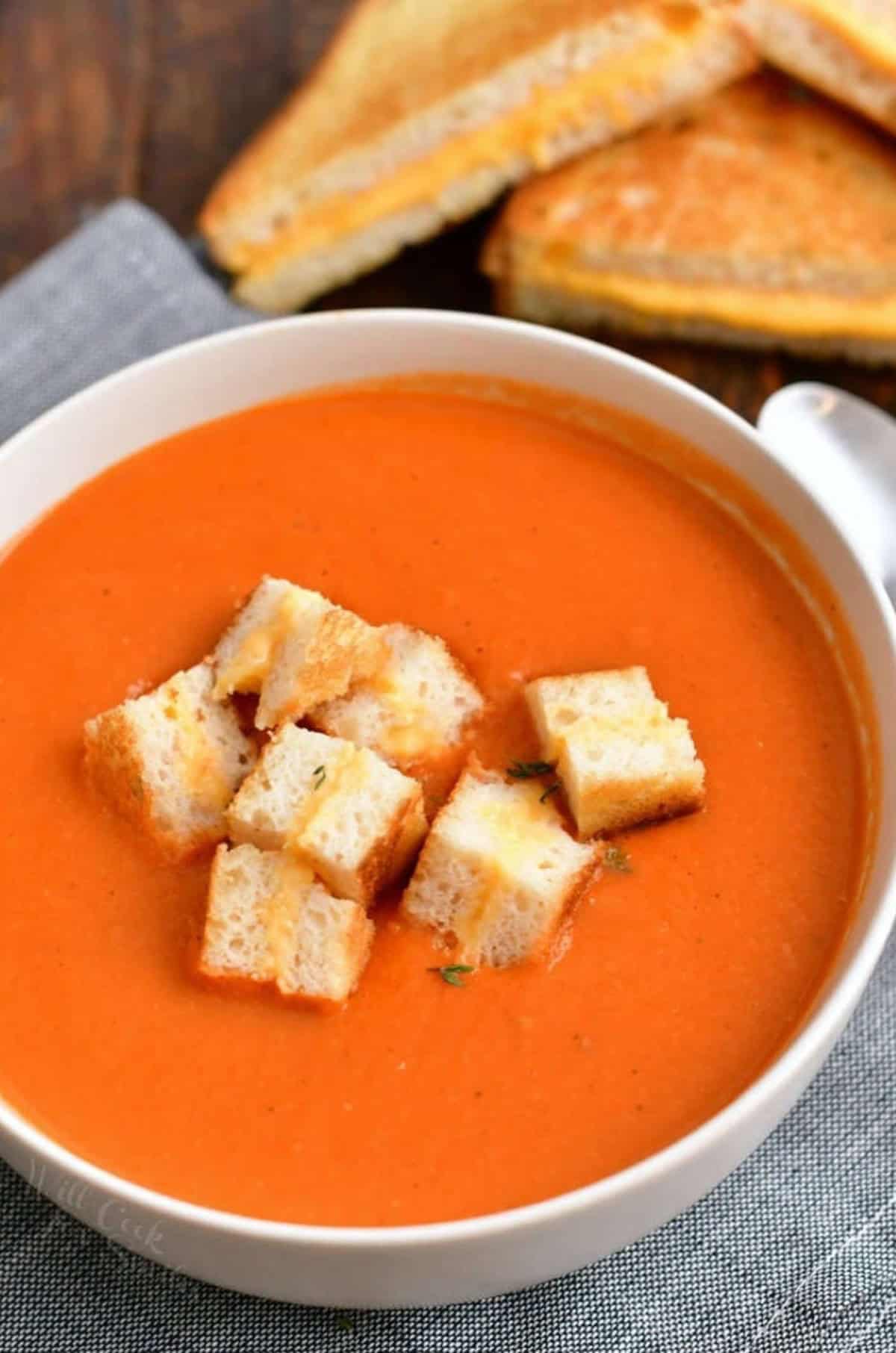 a bowl of classic tomato soup with chopped grilled cheese pieces in it.