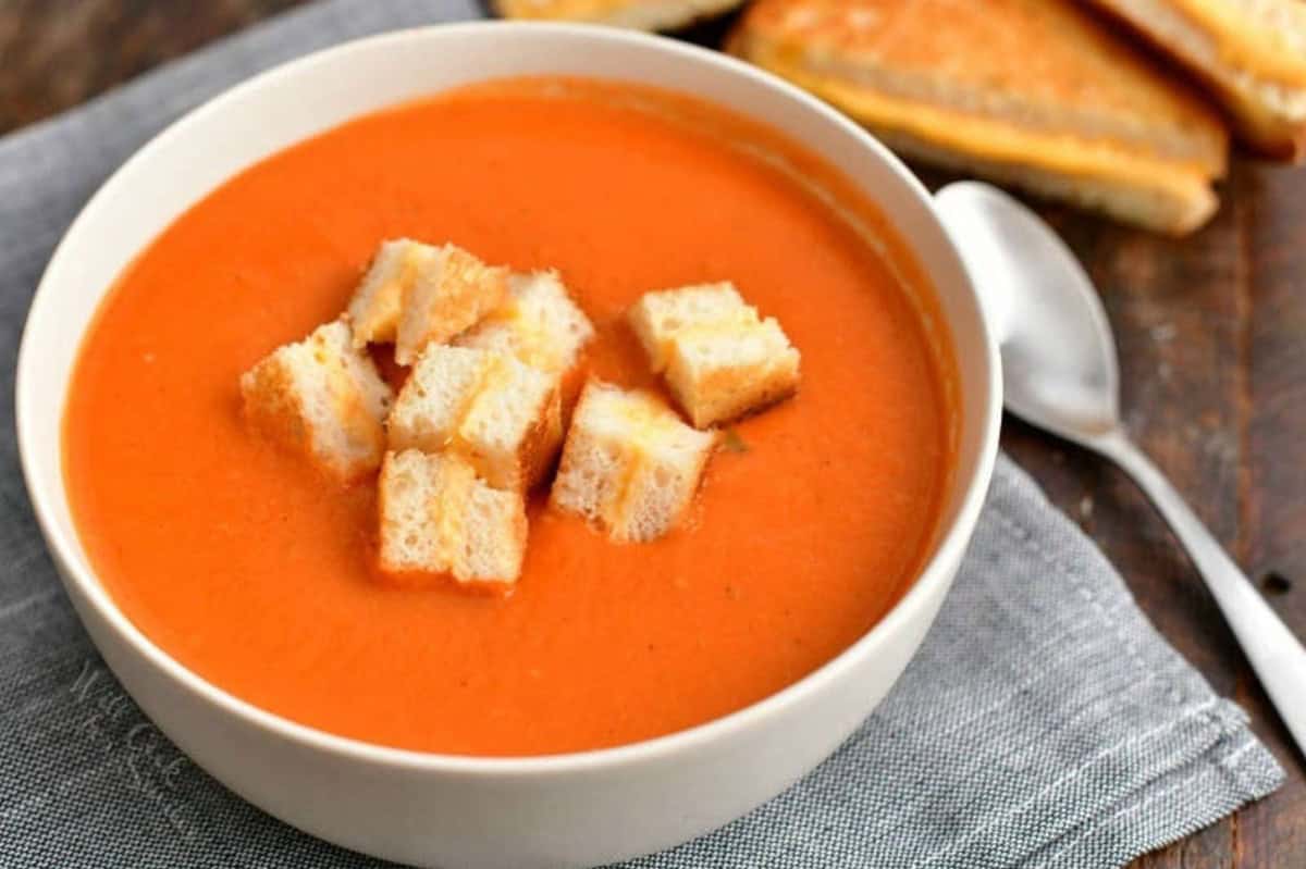 tomato soup in a bowl with some grilled cheese pieces in it.