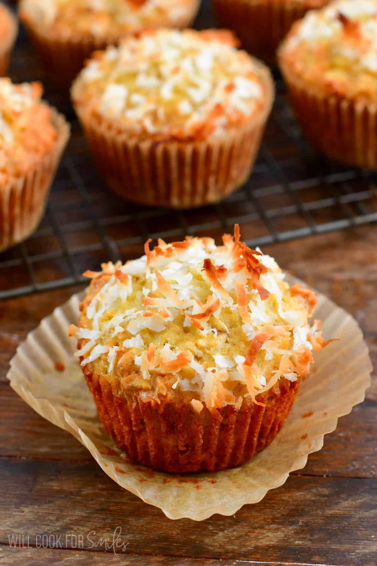 Coconut Oat Muffins with the muffin linner taken off and the rest of the muffins on a wire rack in the background.