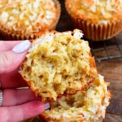 holding a coconut oat muffin that has been torn apart. with the other half on a wood surface