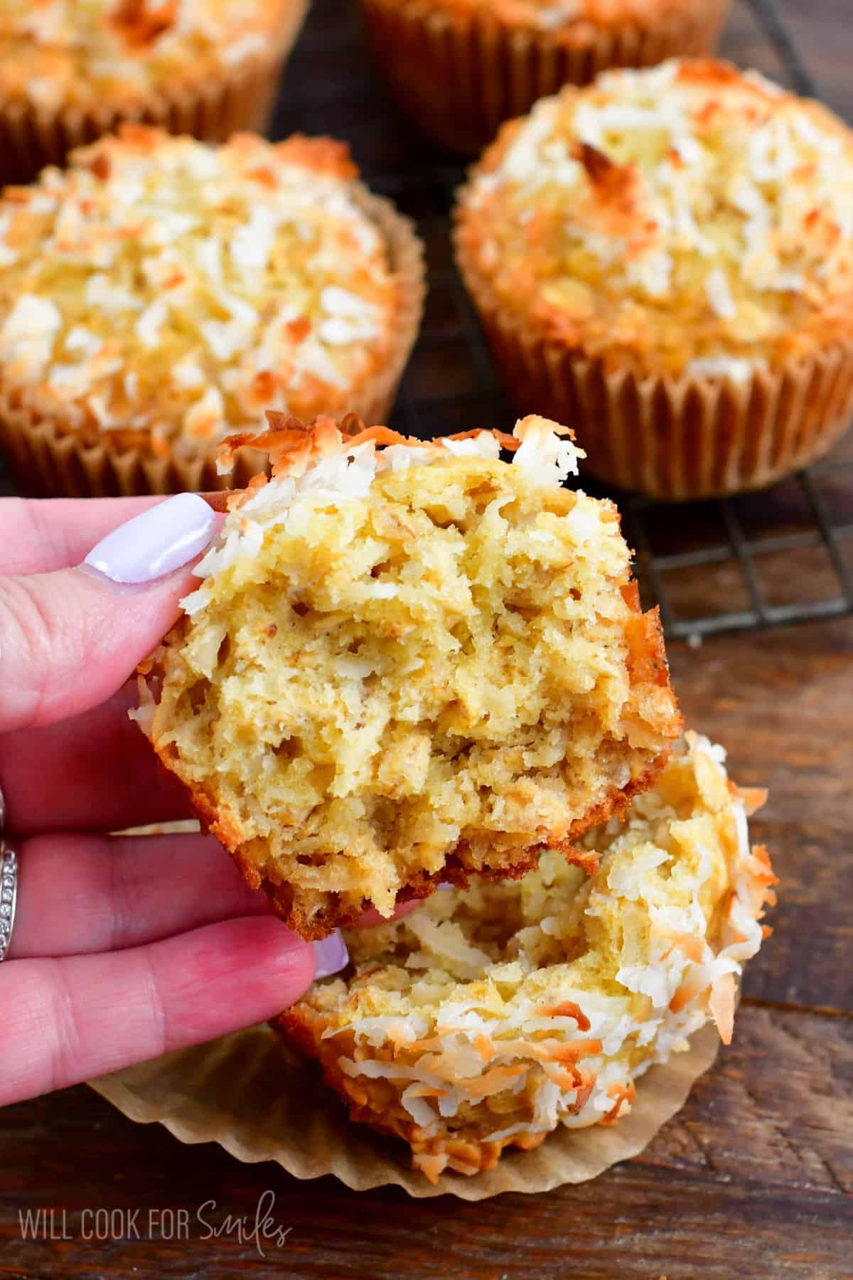 holding a coconut oat muffin that has been torn apart. with the other half on a wood surface