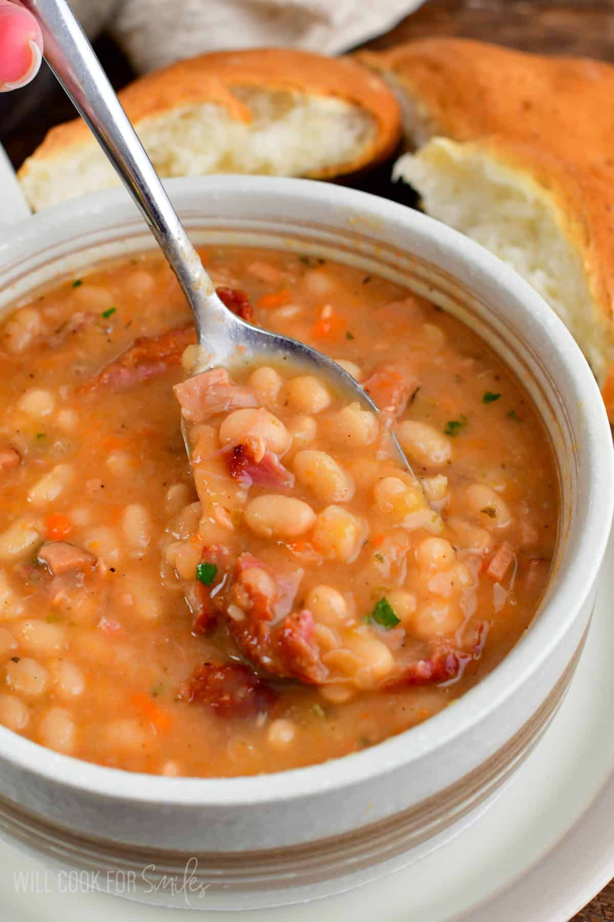 spooning some bean soup from the bowl with bread next to it.