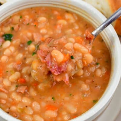 spooning out some ham and bean soup with a silver spoon.