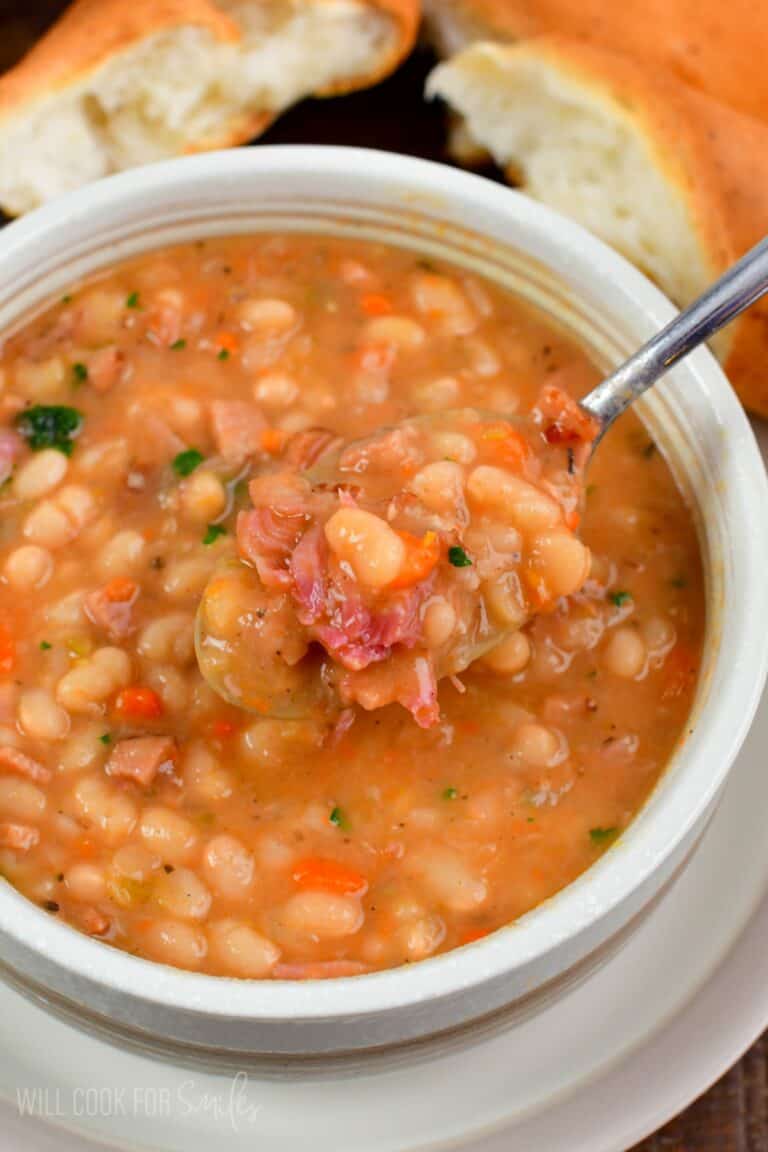 spooning out some ham and bean soup with a silver spoon.