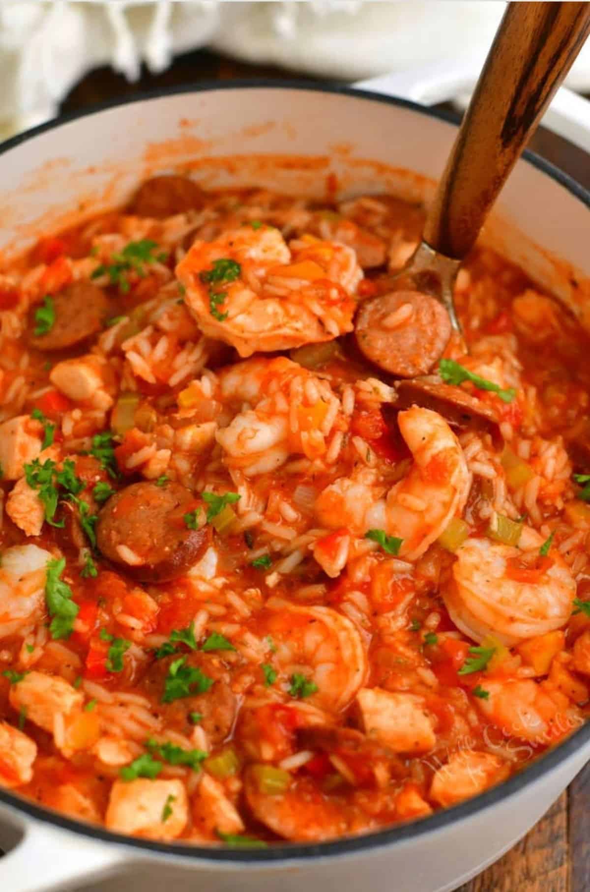 scooping a ladle-full of jambalaya out of the pot using a ladle with a wooden spoon.