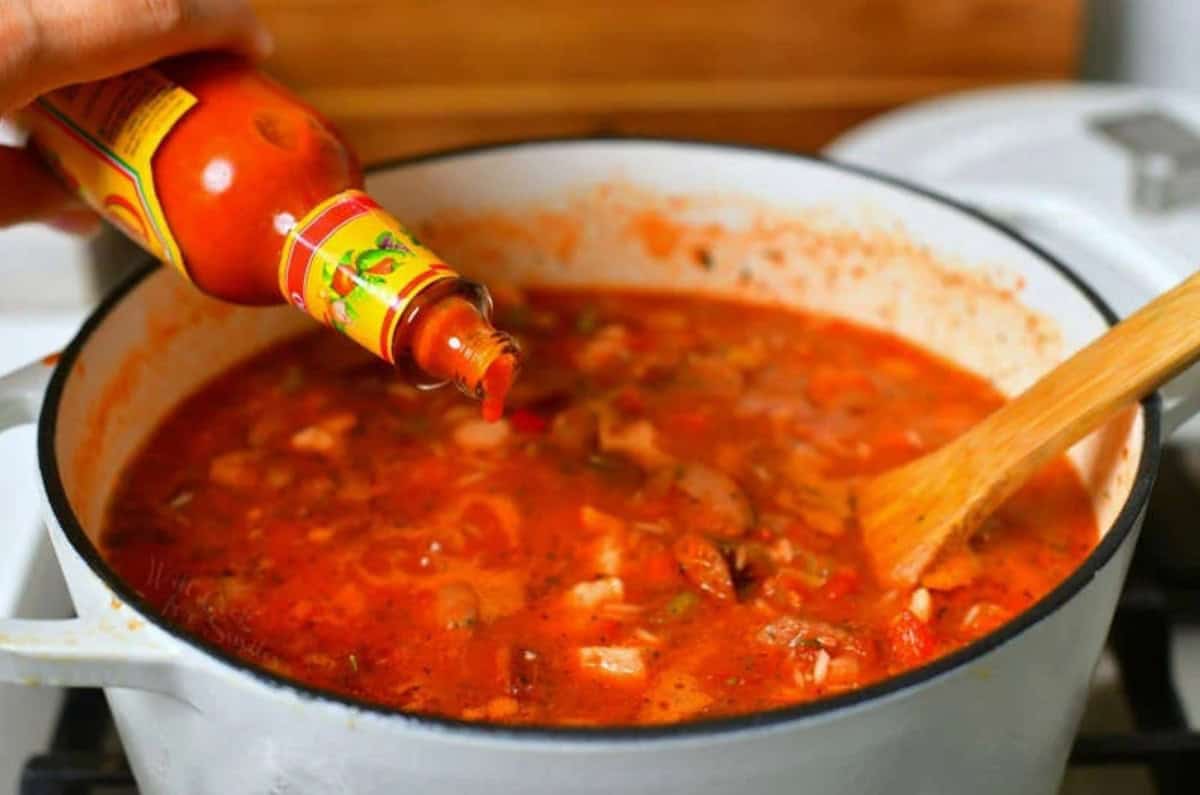 adding a few drops of hot sauce into the pot of jambalaya while it's cooking on the stove.