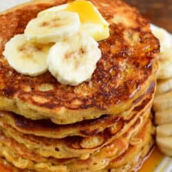 stack of rustic oatmeal pancakes topped with banana slices and butter.