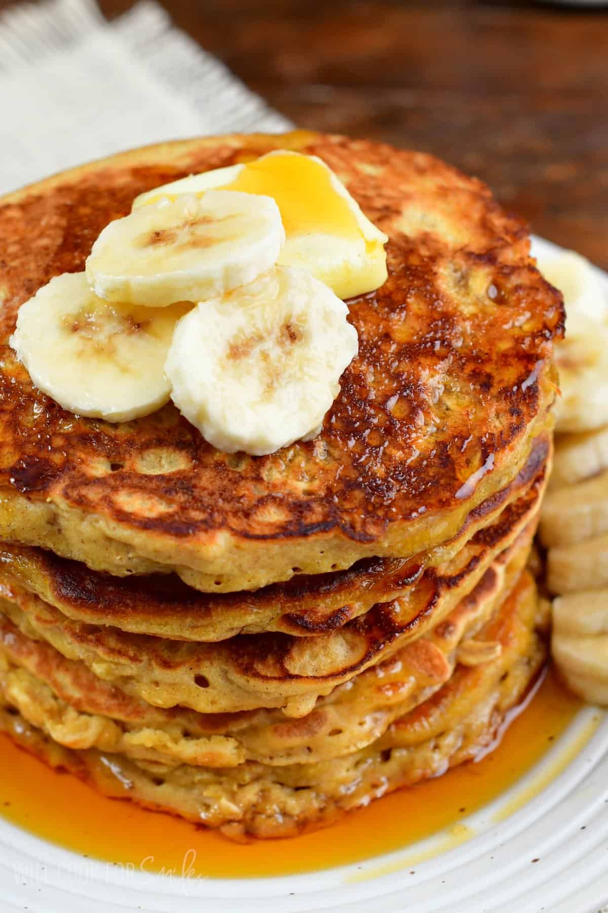 stack of rustic oatmeal pancakes topped with banana slices and butter.