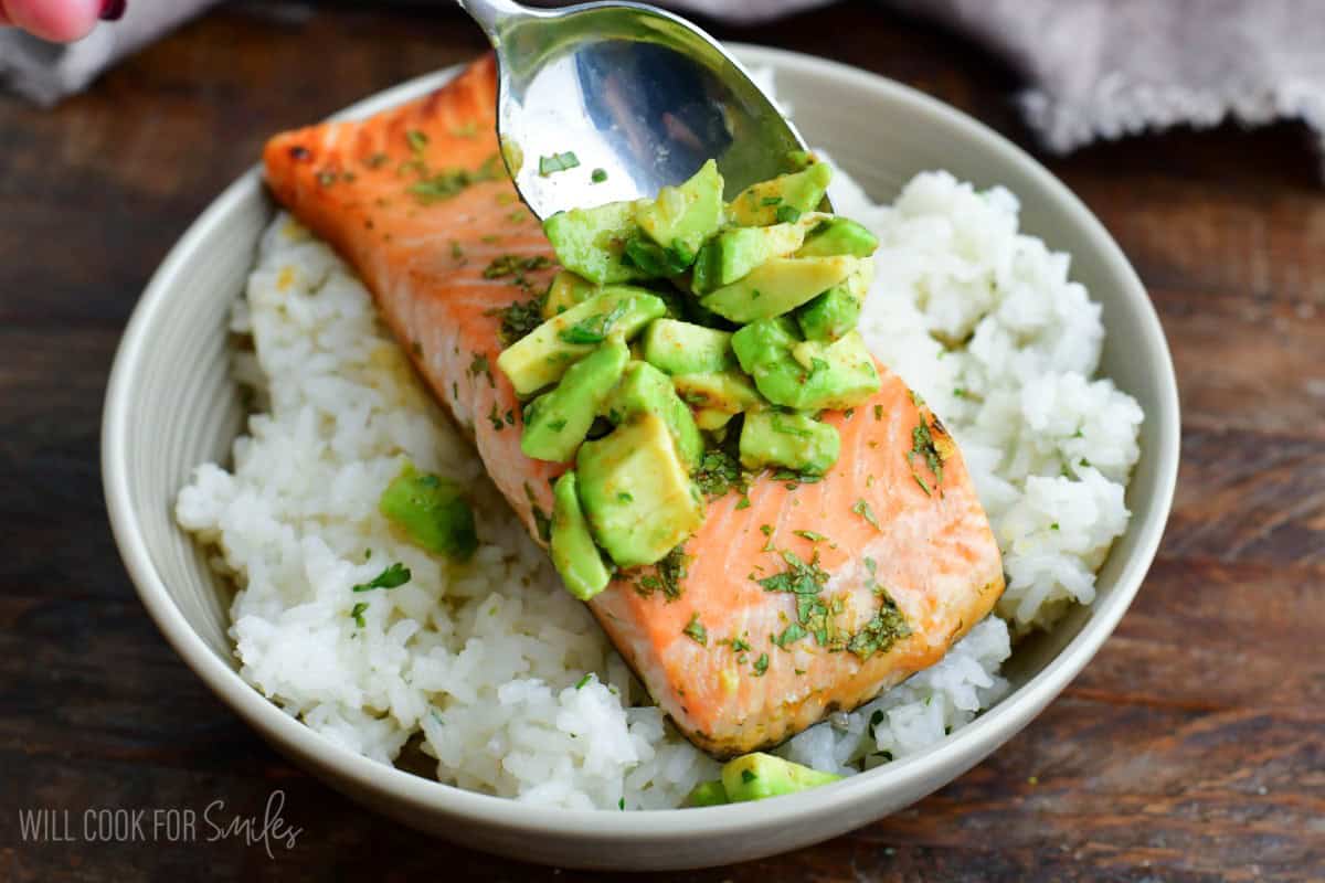 adding some avocado topping on top of salmon in a rice bowl.