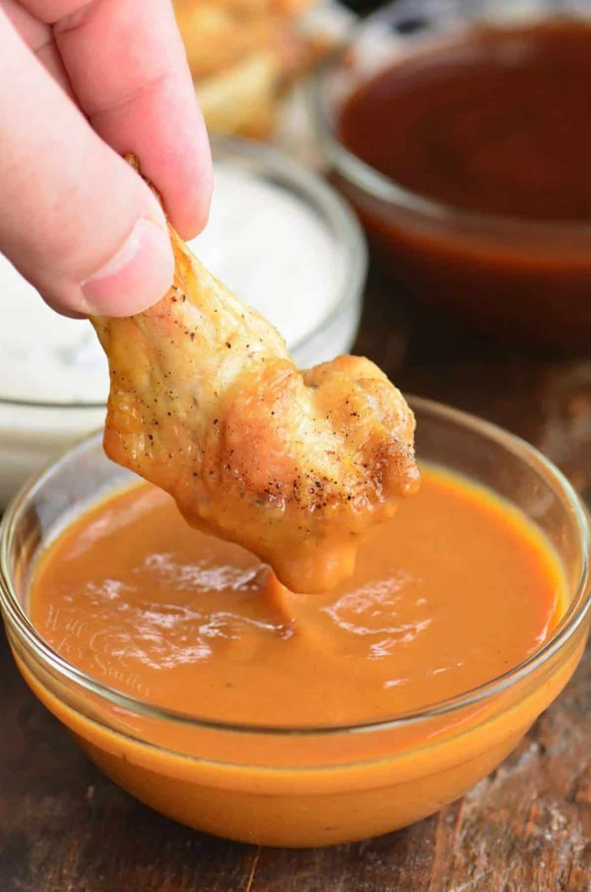 Dipping a baked chicken wing into a bowl of sauce.