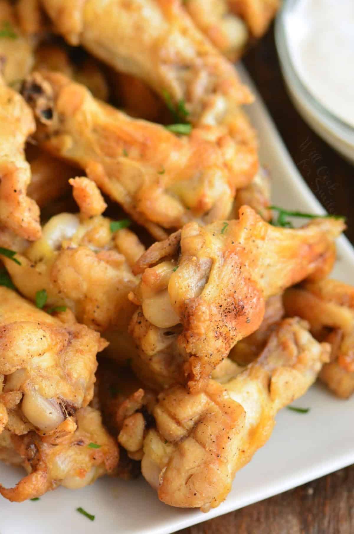 several baked chicken wings on a white plate next to ranch.