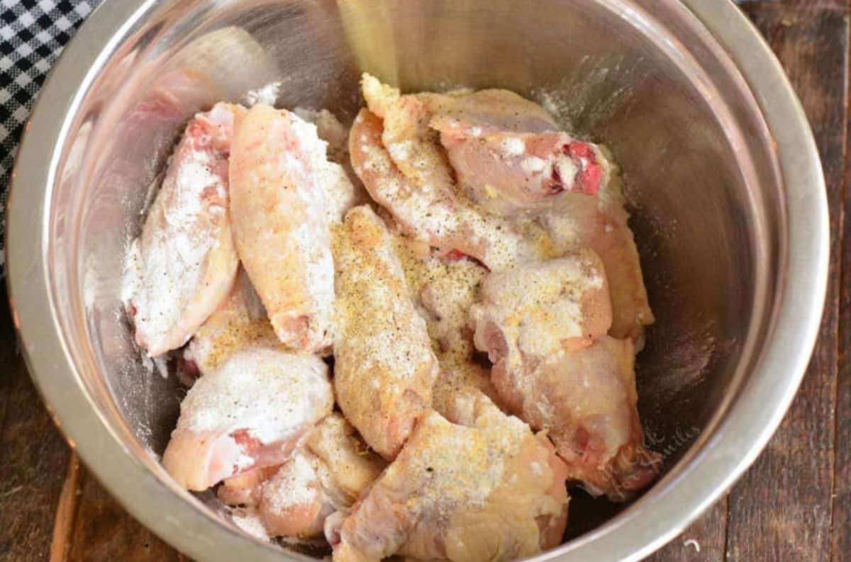 Uncooked chicken wings in a bowl with seasoning.