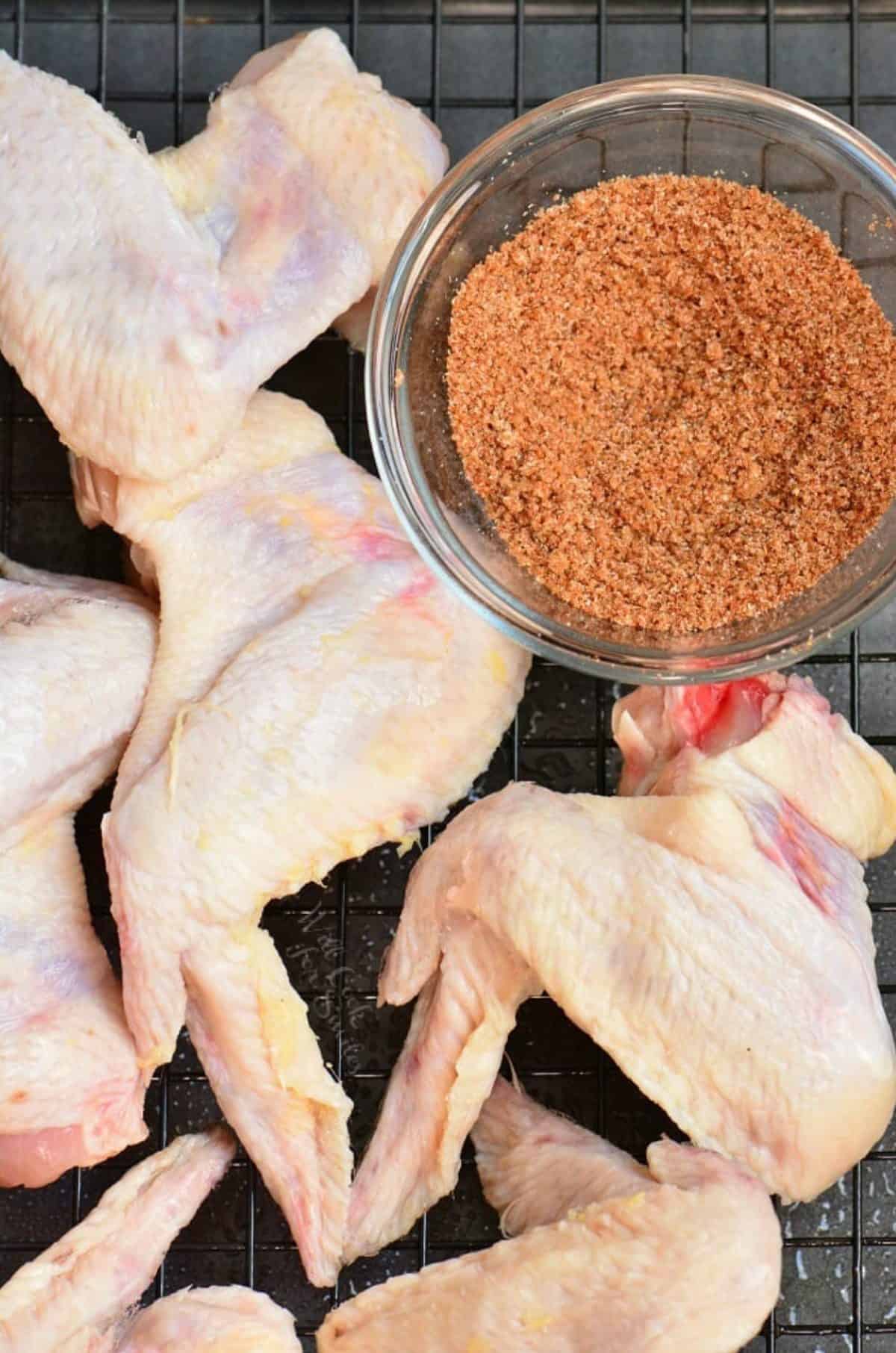 uncooked chicken wings on a wire rack with a bowl of dry rub next to it.