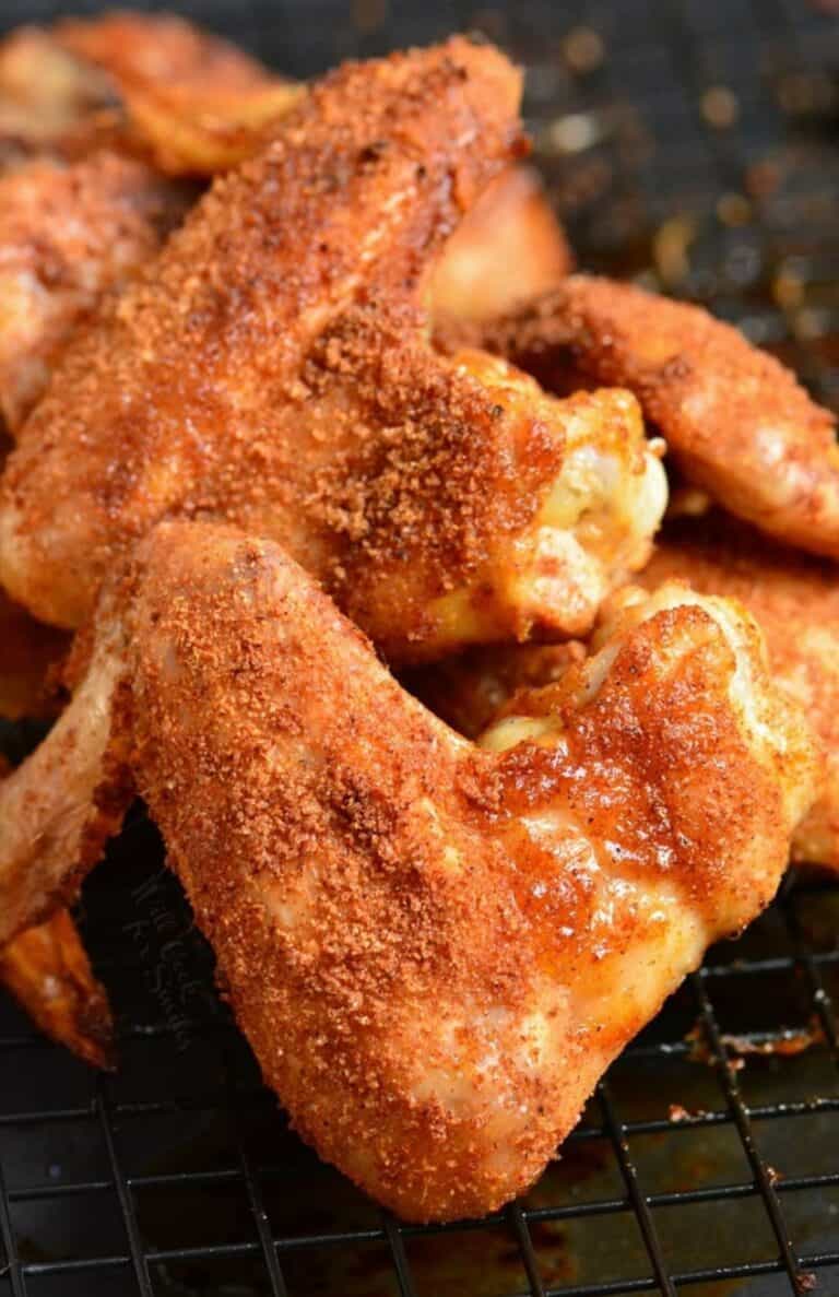 Baked chicken wings with dry rub stacked up on a wire rack.