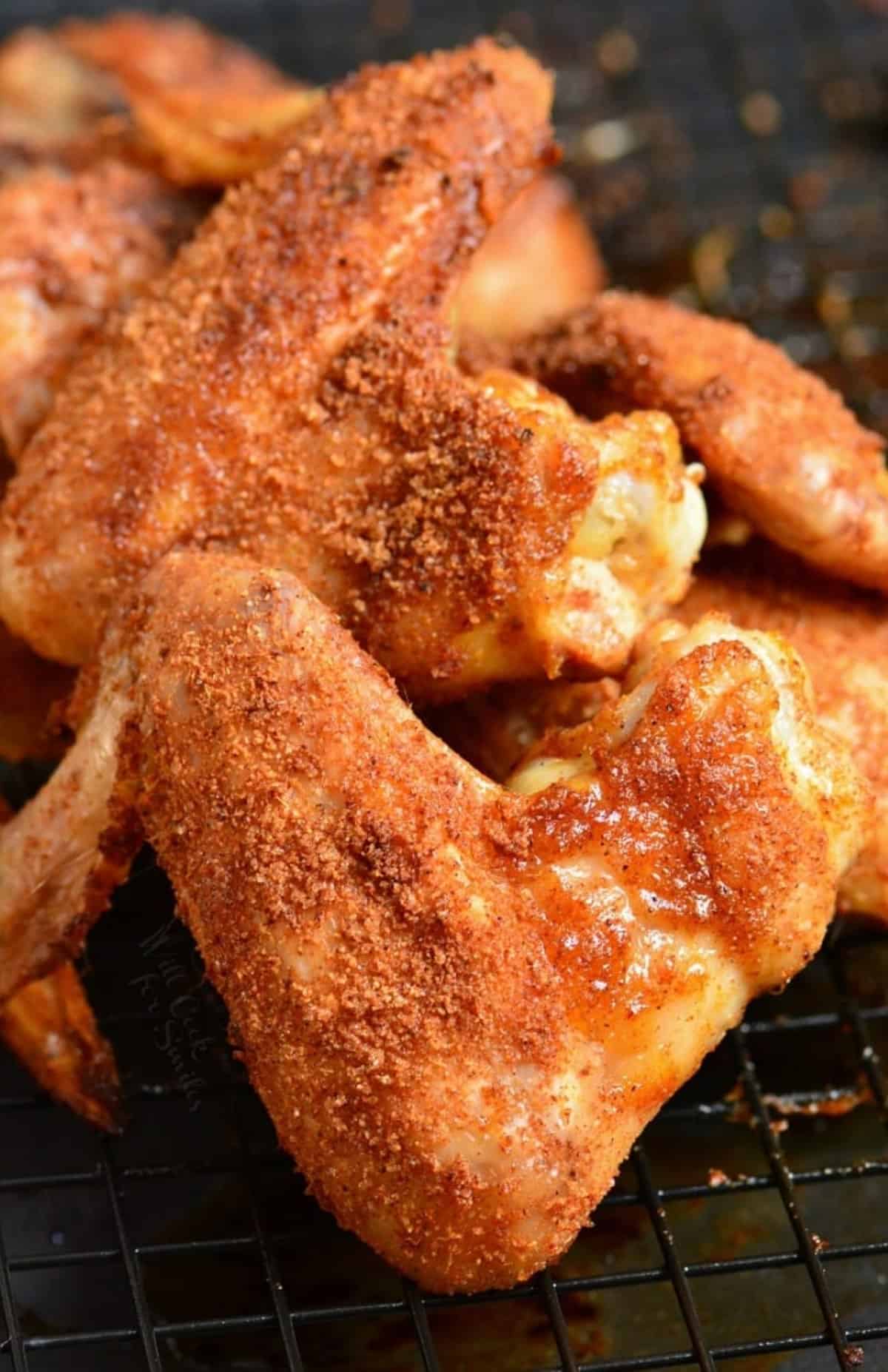 Baked chicken wings with dry rub stacked up on a wire rack.