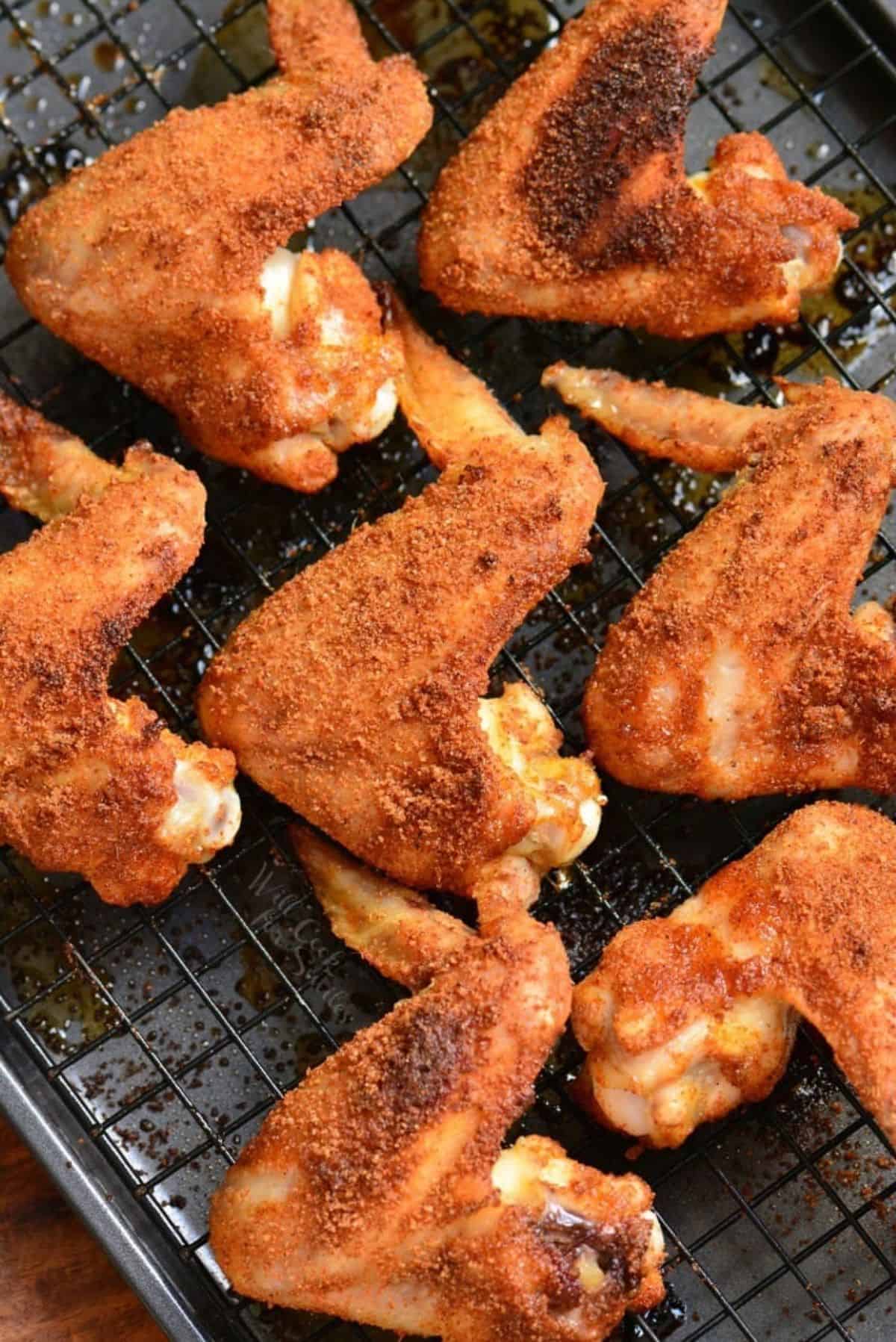 multiple baked chicken wings with dry rub on a wire rack.