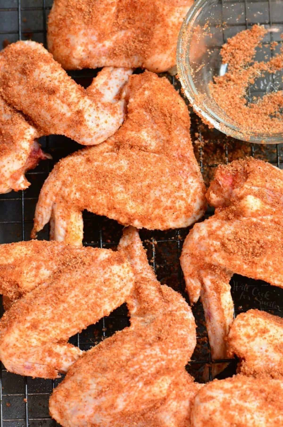 uncooked chicken wings with dry rub on them on a wire rack.