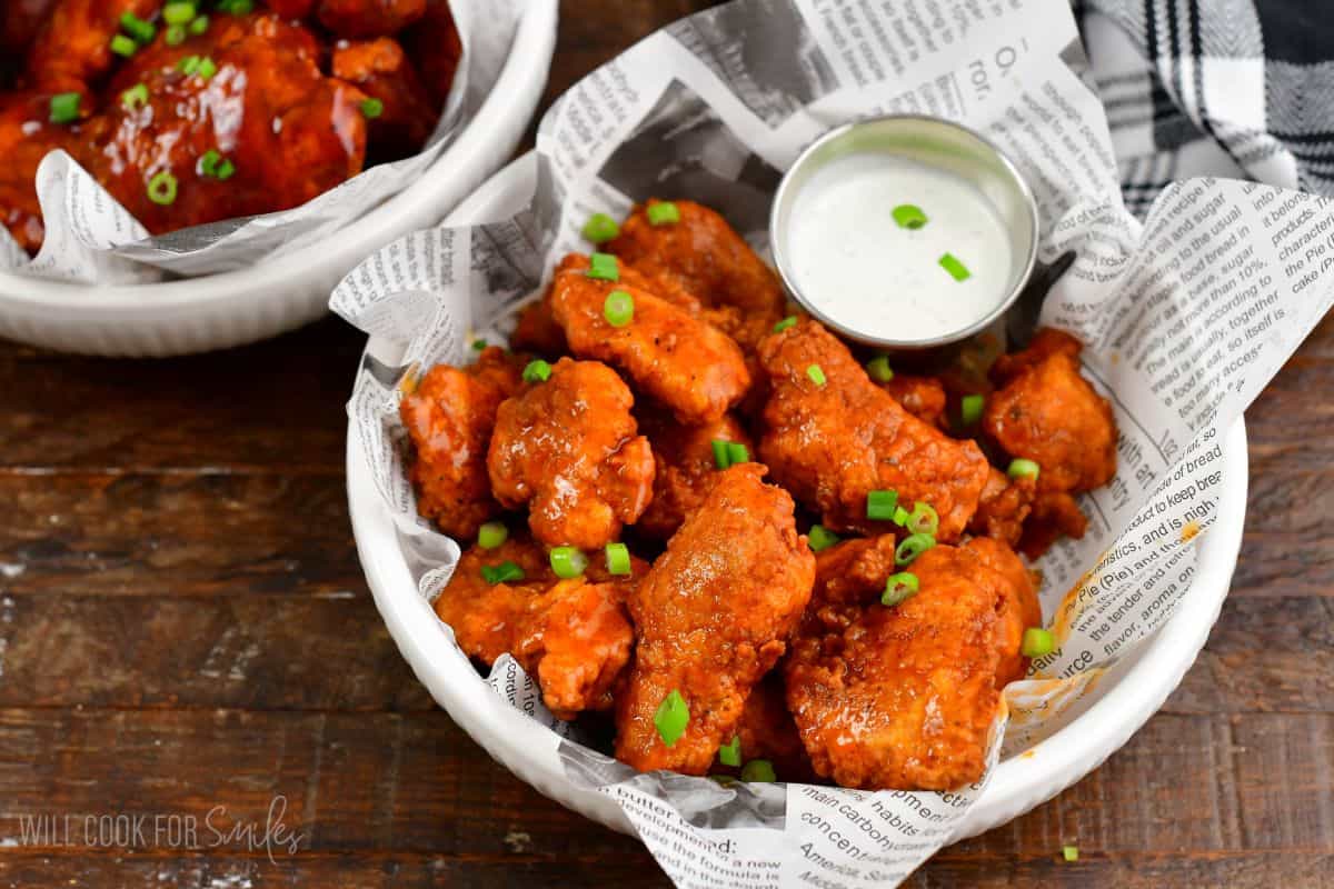 several buffalo sauce boneless wings in a bowl with a side of ranch dressing.