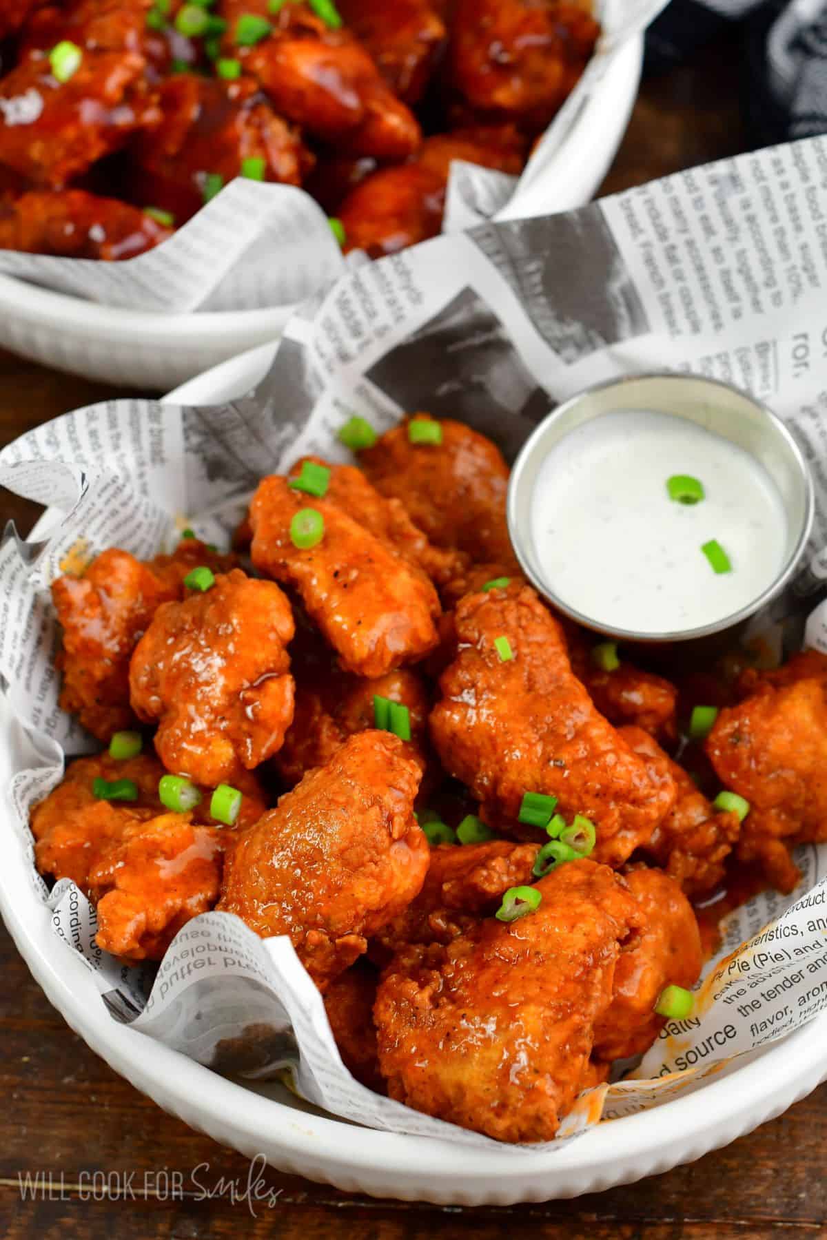 buffalo sauce coated boneless chicken wings with green onion on top.