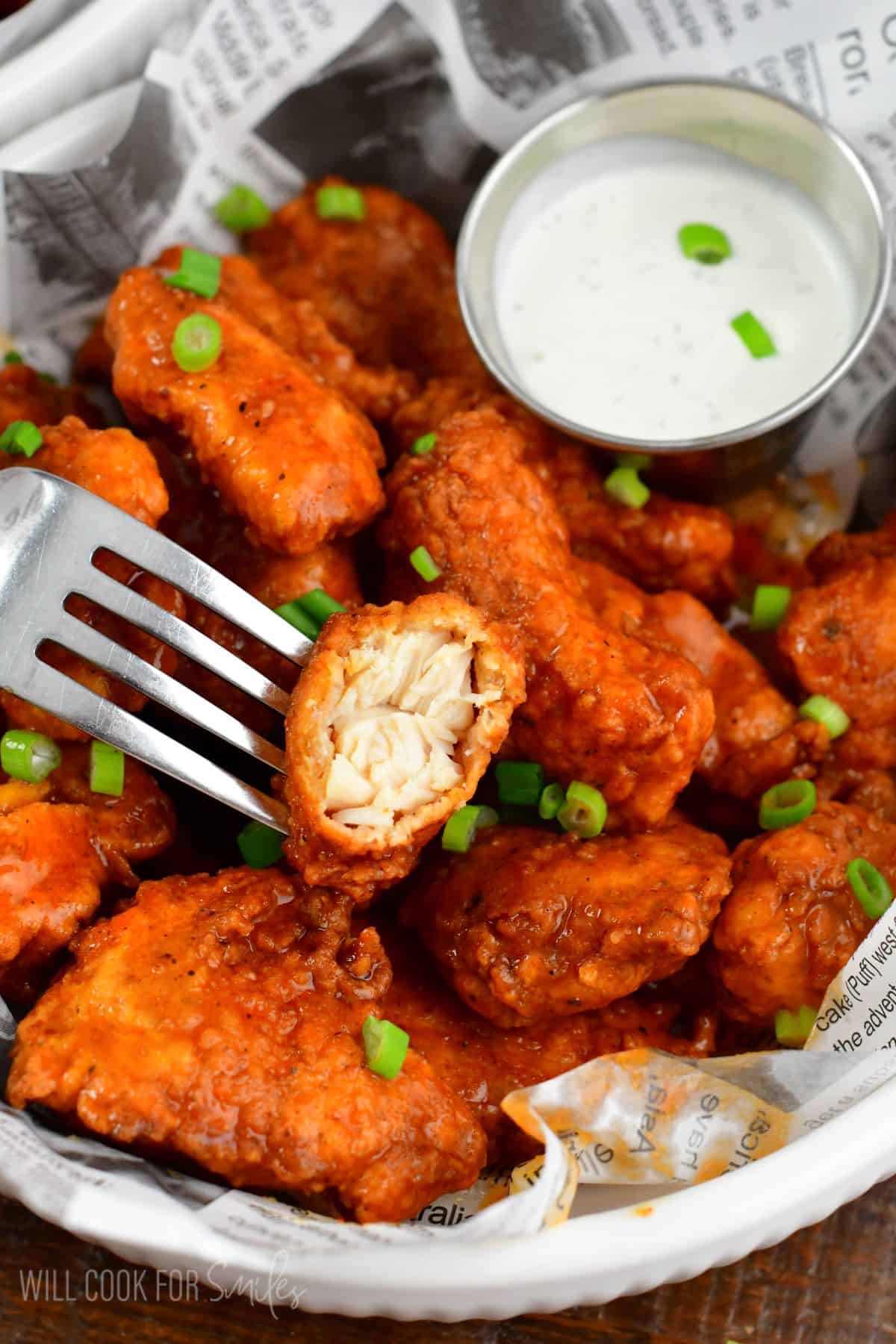 boneless wings in buffalo wing sauce in a bowl with one bite taken out of one wing.