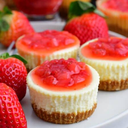 three mini cheesecakes on the plate topped with strawberry topping.