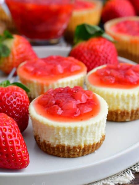 three mini cheesecakes on the plate topped with strawberry topping.