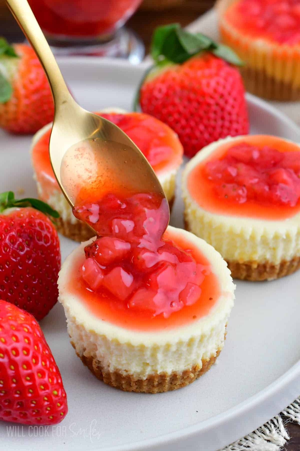 adding some strawberry topping onto a mini NY style cheesecake.