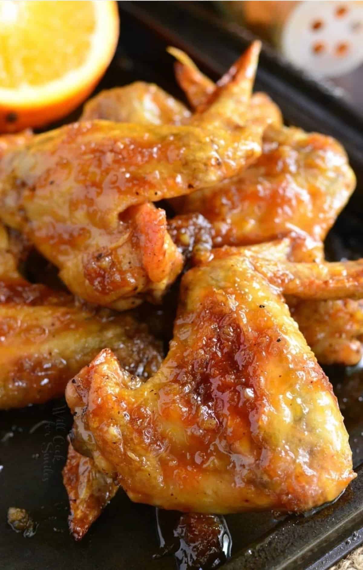 Baked chicken wings with an orange glaze piled up on a baking sheet.