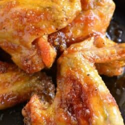 Orange glazed chicken wings stacked up on a baking sheet.