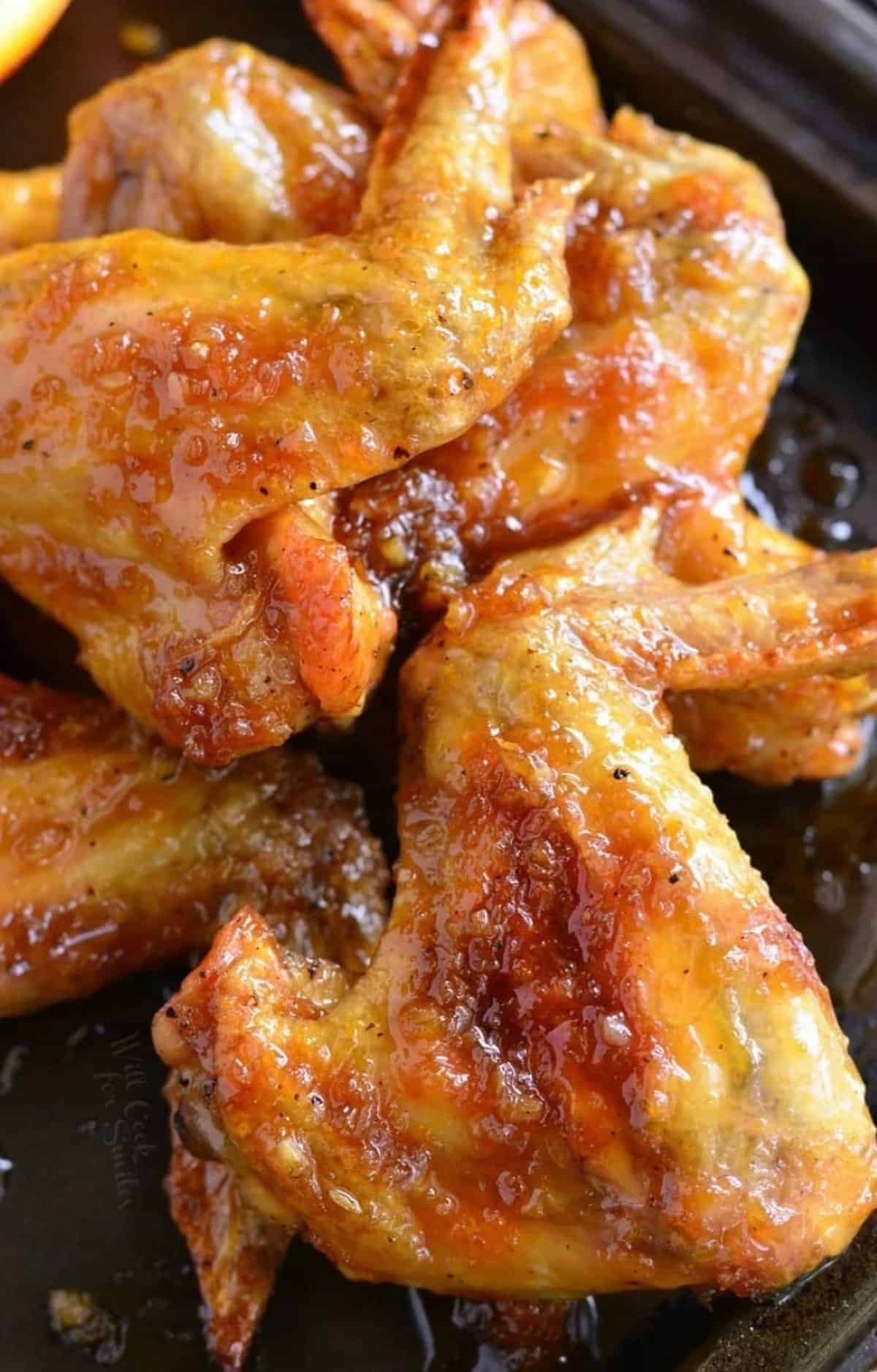 Orange glazed chicken wings stacked up on a baking sheet.